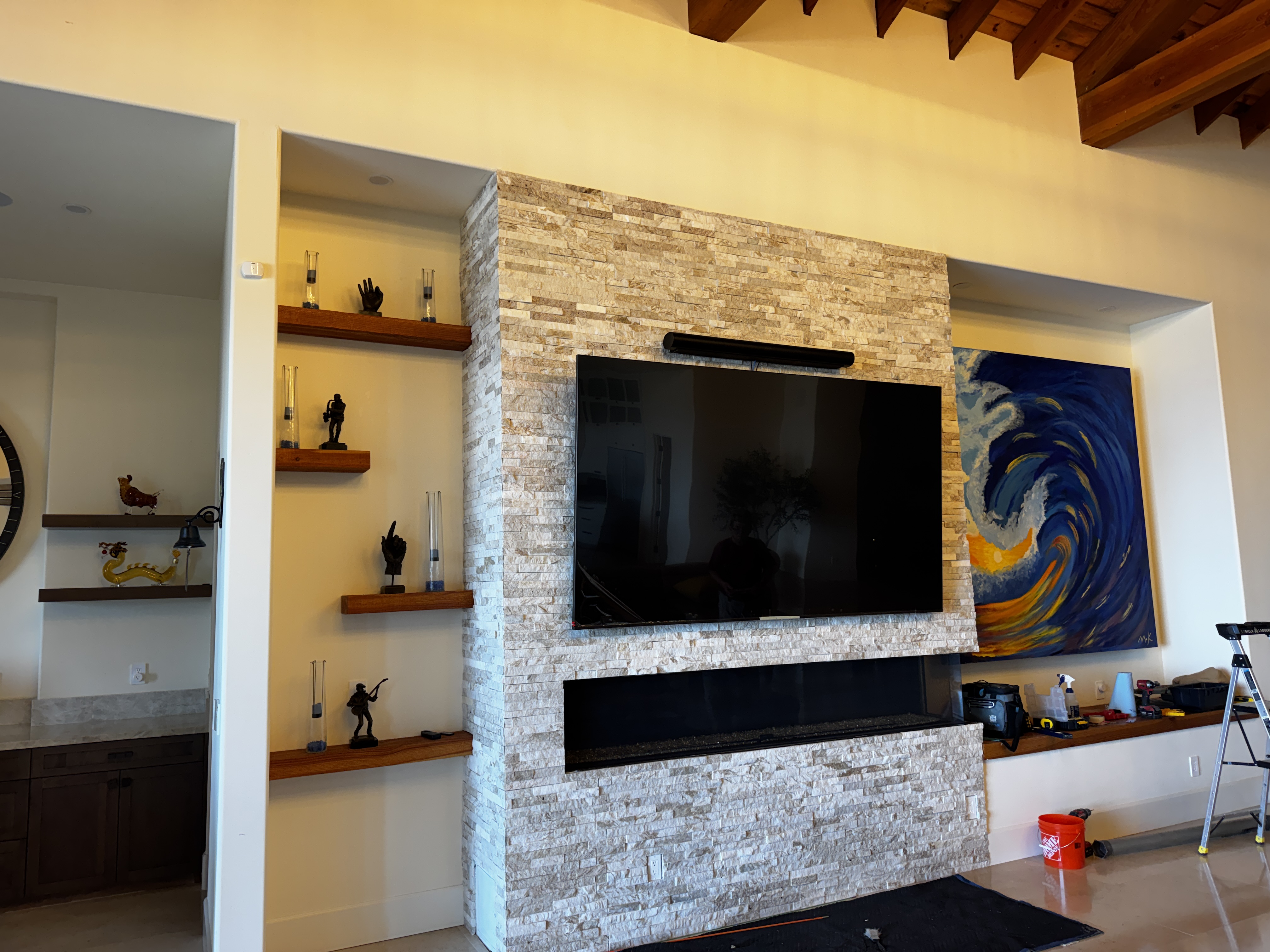 Wide view of living room with 100-inch TV on stone fireplace wall, built-in shelving, original artwork
